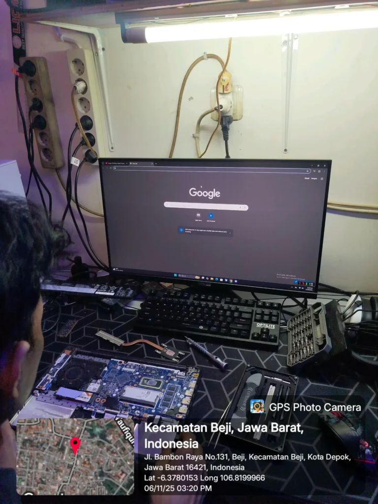 Foto meja kerja teknisi dengan sebuah laptop yang sedang dibongkar untuk pengecekan masalah performa lemot. Terlihat motherboard, modul RAM, dan penyimpanan yang sedang diperiksa. Di meja terdapat kuas pembersih, set obeng presisi, dan beberapa alat servis. Sebuah monitor menampilkan desktop Windows, menunjukkan proses diagnosa. Area kerja dikelilingi kabel, lampu kerja, dan peralatan teknisi lainnya
