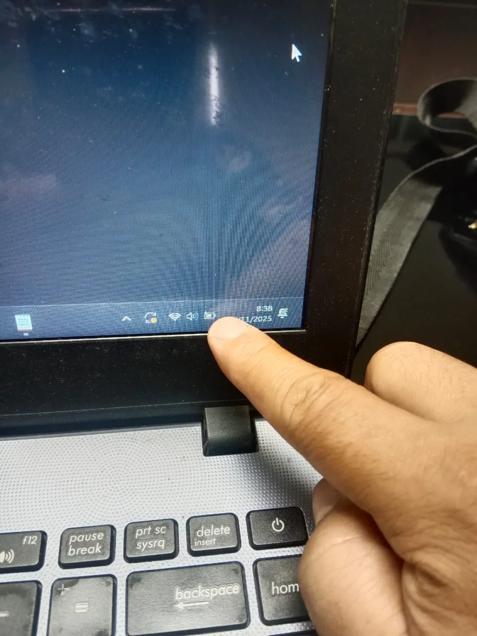 “Jari tangan menunjuk ikon baterai di pojok kanan bawah layar laptop yang terbuka, keyboard hitam-abu dan engsel layar terlihat jelas.”