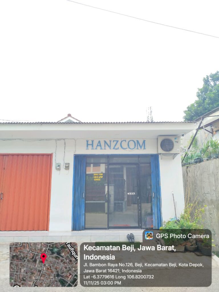 Bangunan HanzCom Laptop dari sudut depan dengan rollingdor biru langit yang cerah. Lokasi berada di Jl. Bambon Raya, Beji, Depok, dekat dengan pemukiman dan akses jalan lingkungan.