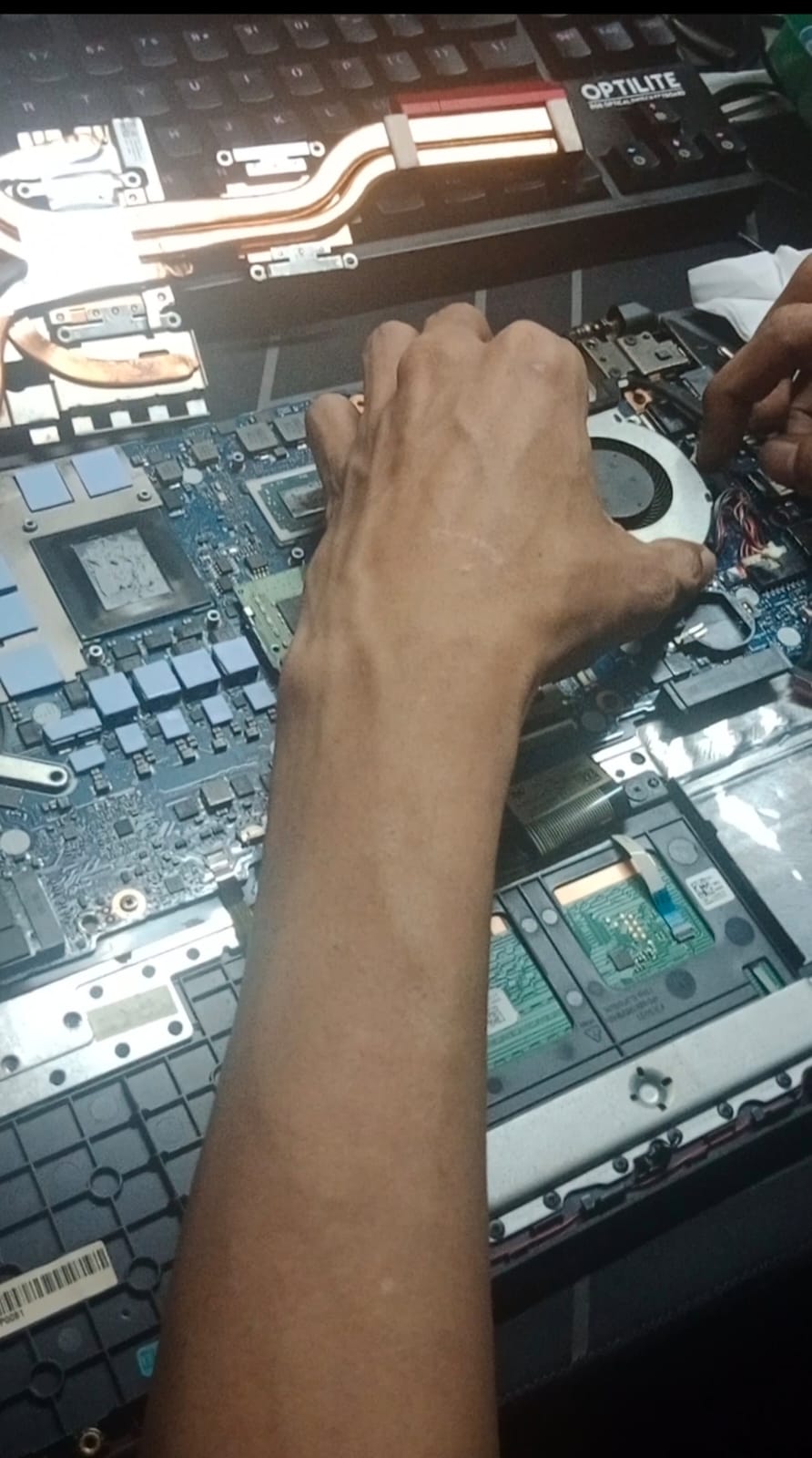 “Pemeriksaan manual pada motherboard laptop, terlihat jalur VRM, pendingin tembaga, socket CPU, dan kipas internal saat teknisi melakukan diagnosa detail.”