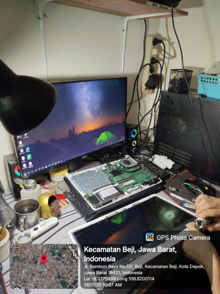 “Laptop dengan motherboard terbuka sedang diperiksa komponen VRM dan konektor layar; panel LCD dilepas, obeng presisi terlihat di tangan teknisi, dengan monitor eksternal dan alat solder di meja kerja.”