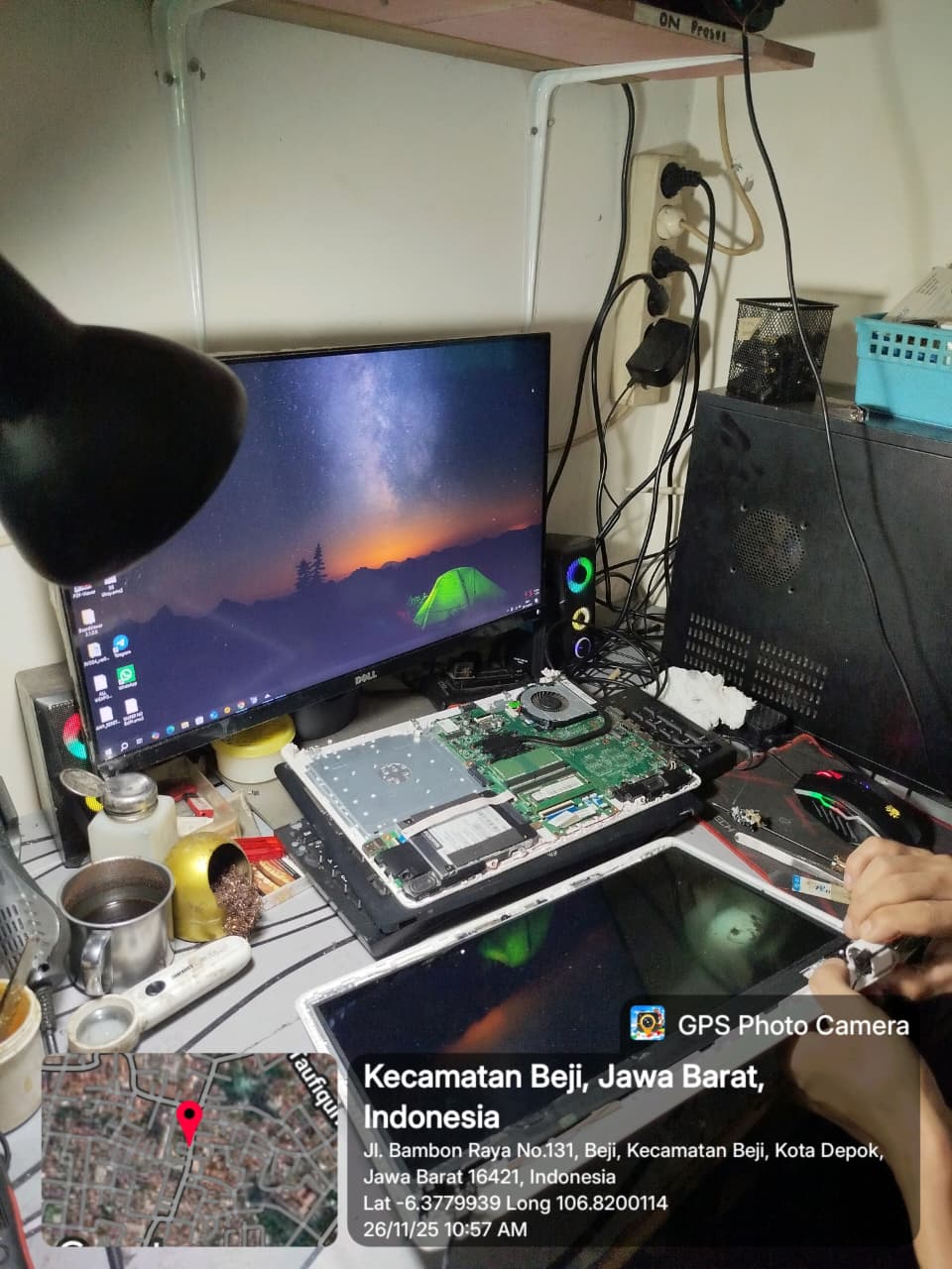 “Laptop dengan motherboard terbuka sedang diperiksa komponen VRM dan konektor layar; panel LCD dilepas, obeng presisi terlihat di tangan teknisi, dengan monitor eksternal dan alat solder di meja kerja.”